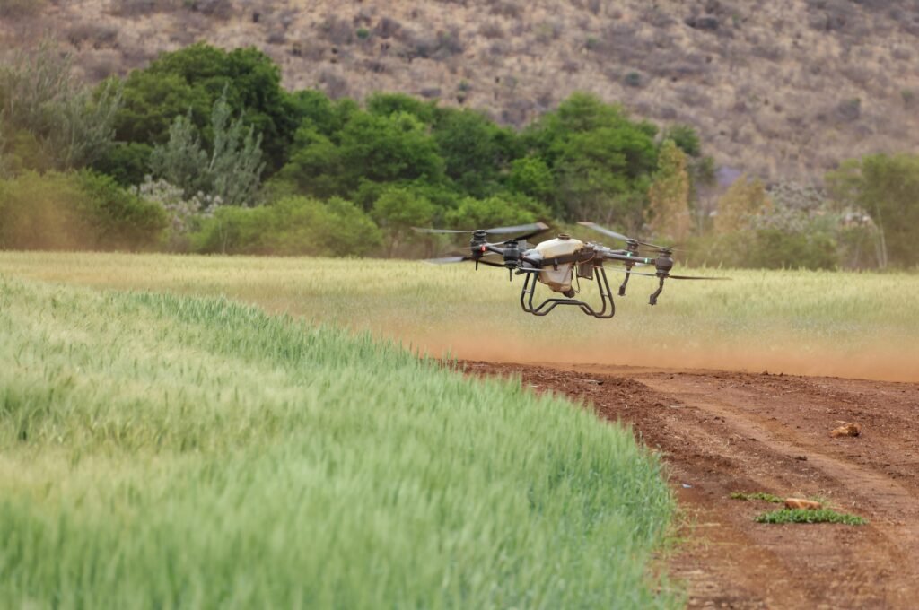 Aerial drone surveying vast green agricultural fields in a rural landscape under a clear blue sky.