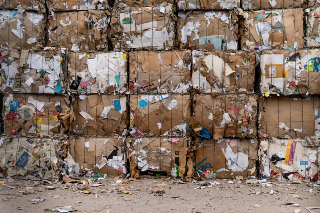 A large pile of discarded household garbage and waste materials sits on a dirt field under an overcast sky, illustrating the environmental impact of poor waste management.
