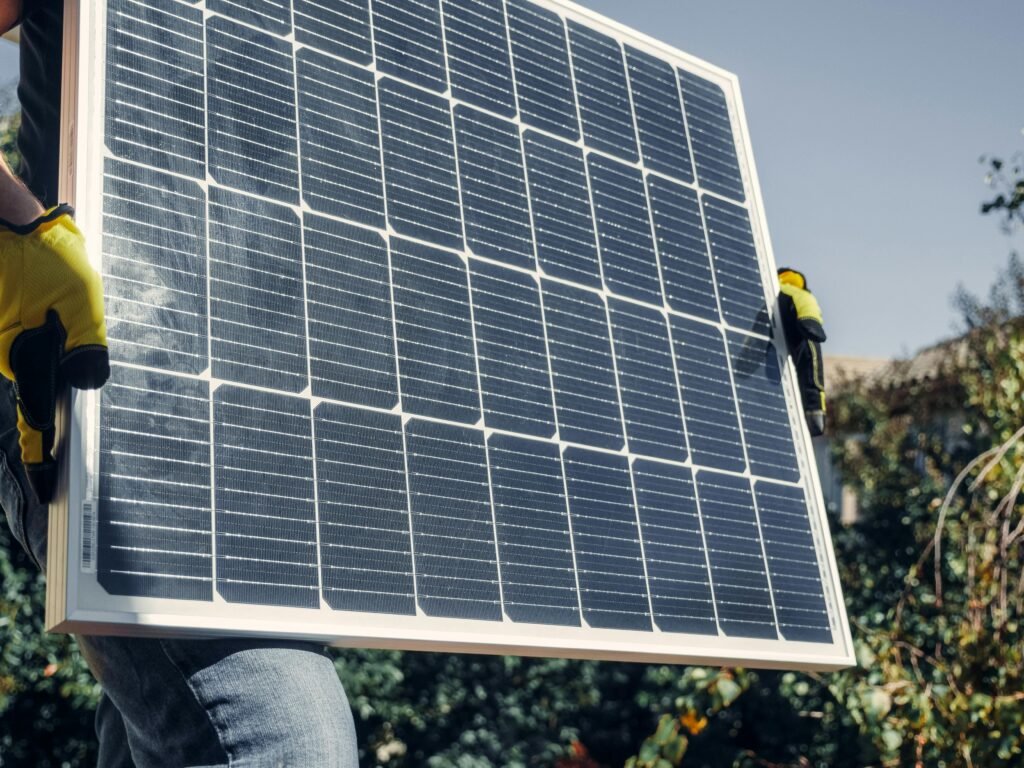 Vibrant green solar panel held by hands against clear sky, representing accessible low-tech renewable energy solutions.