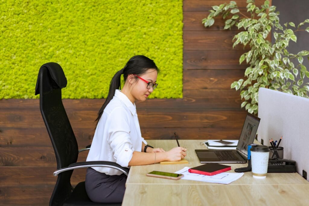 Professional woman focused at modern office desk with laptop and papers, symbolizing quiet corporate work amid sustainability silence.