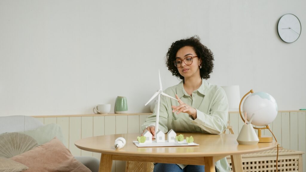 Young woman smiling confidently while holding a small windmill model, representing hands-on renewable energy innovation and youth-led sustainable technology.