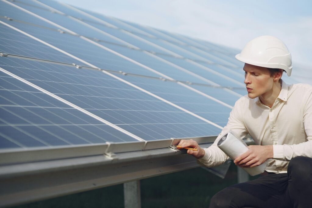 Solar technician in safety gear closely inspecting large photovoltaic panels on a sunny day, highlighting routine maintenance for efficient renewable energy systems.